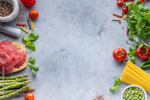 Frame for Italian food. Ingredients for pasta. Cherry tomatoes, meat, spaghetti pasta, garlic, Basil, asparagus, broccoli and spices on a grey grunge background, copy space, top view 