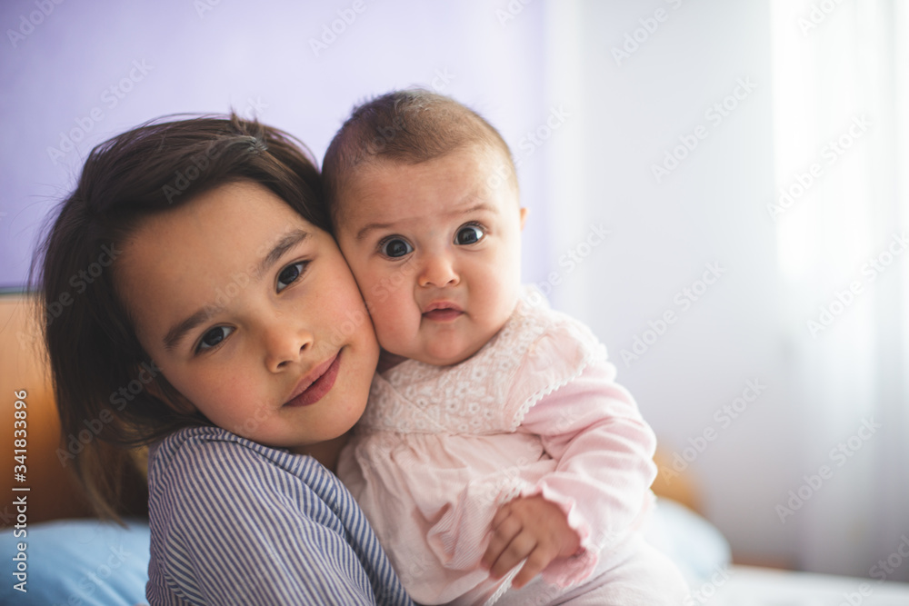 Big little sister holding her little sister and looking at camera with funny faces Big little sister holding her little sister and looking at camera with funny faces
