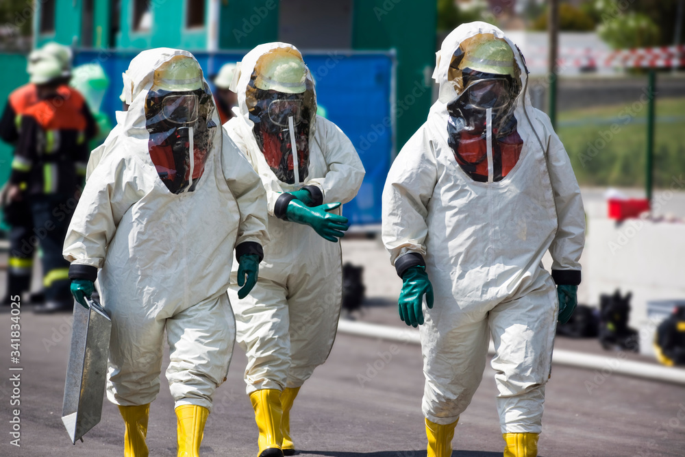 Three men in protective gear disinfecting contaminated areas or cleaning up after chemical or radiation accident. The inflatable gear protects against contamination with viruses, radioactive particles - obrazy, fototapety, plakaty 