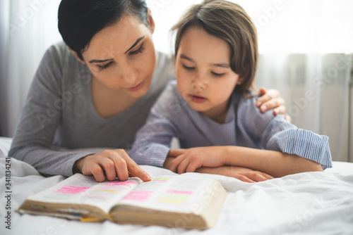 Photos Mother and her daughter reading from bible and praying in their knees near the b