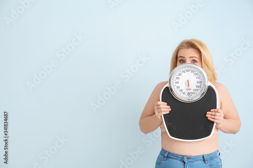 Troubled overweight woman with scales on color background. Weight loss concept photo