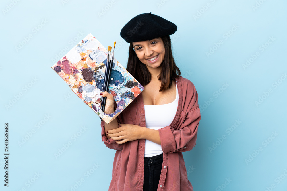Fototapeta premium Young artist woman holding a palette over isolated blue background laughing.