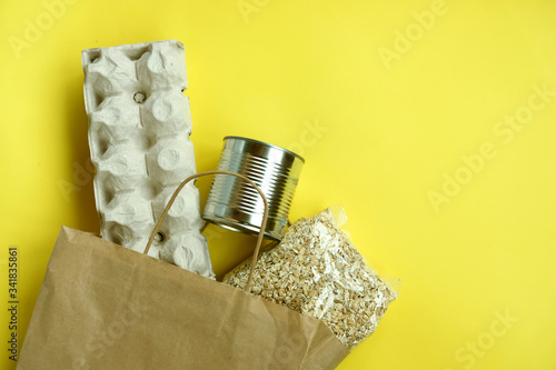 Food in a paper bag: eggs, canned food and oat groats on a yellow background