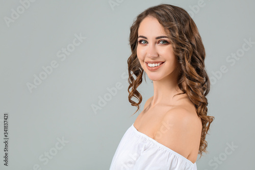 Beautiful young woman with curly hair on grey background