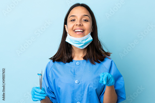 Young brunette mixed race dentist woman holding tools over isolated background surprised and pointing front