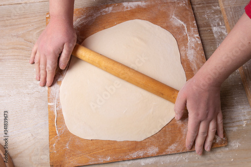 Female hands rolling dough on a cutting board with a rolling pin. Cooking at home.