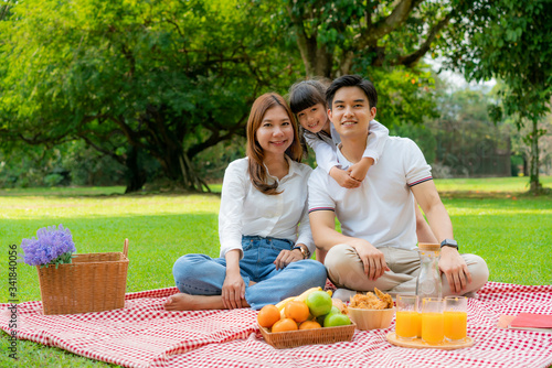 Asian teen family happy holiday picnic moment in the park with father, mother and daughter looking at camera and smile to happy spend vacation time togerter in green garden with friut and food.. photo