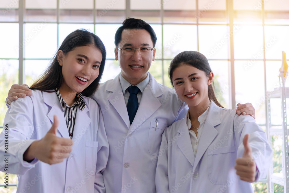 Successful group of chemical showing thumbs up while standing together in the laboratory. Team science people wear white coat holding thumbs up while looking at camera. Teamwork concept. Successful group of chemical showing thumbs up while standing together in the laboratory. Team science people wear white coat holding thumbs up while looking at camera. Teamwork concept.
