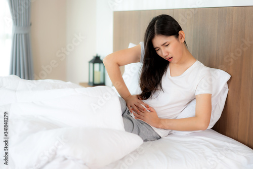 Asian woman unhappy lying on the bed looking sick, suffers from stomach ache in the bedroom, stomachache because of menstruation and eating spoiled food, Chronic gastritis. 