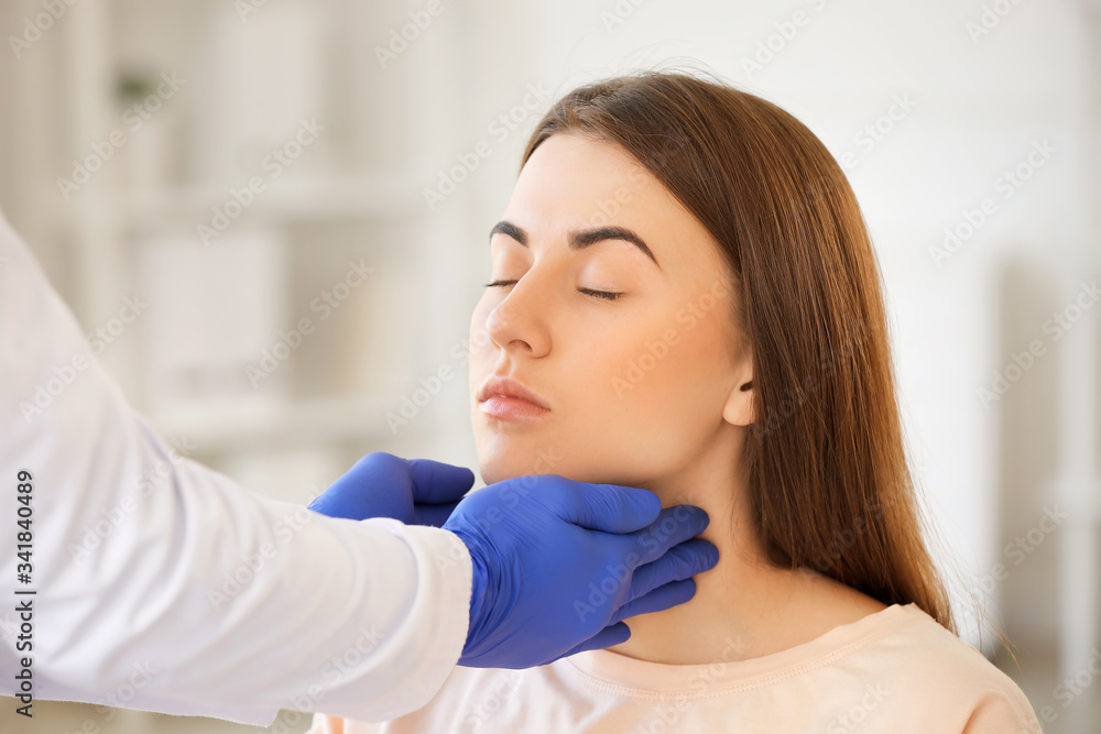 Endocrinologist examining throat of young woman in clinic Endocrinologist examining throat of young woman in clinic