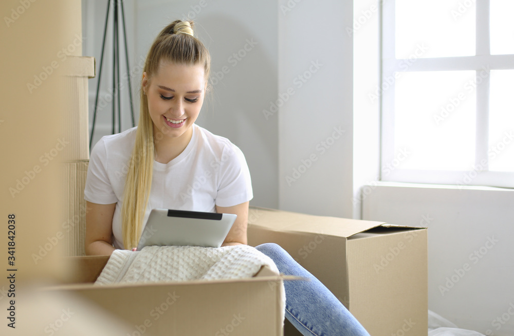 A beautiful single young woman unpacking boxes and moving into a new home. A women look at here tablet A beautiful single young woman unpacking boxes and moving into a new home. A women look at here tablet