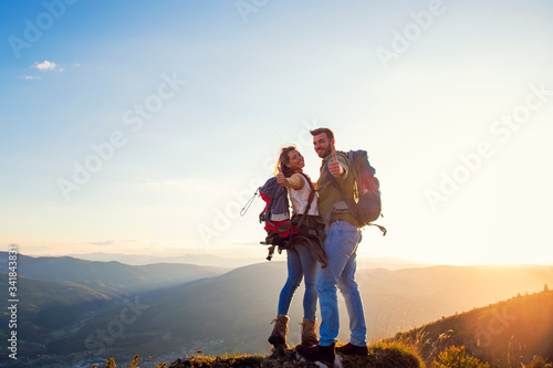 happy couple man and woman tourist at top of mountain at sunset outdoors during a hike in summer