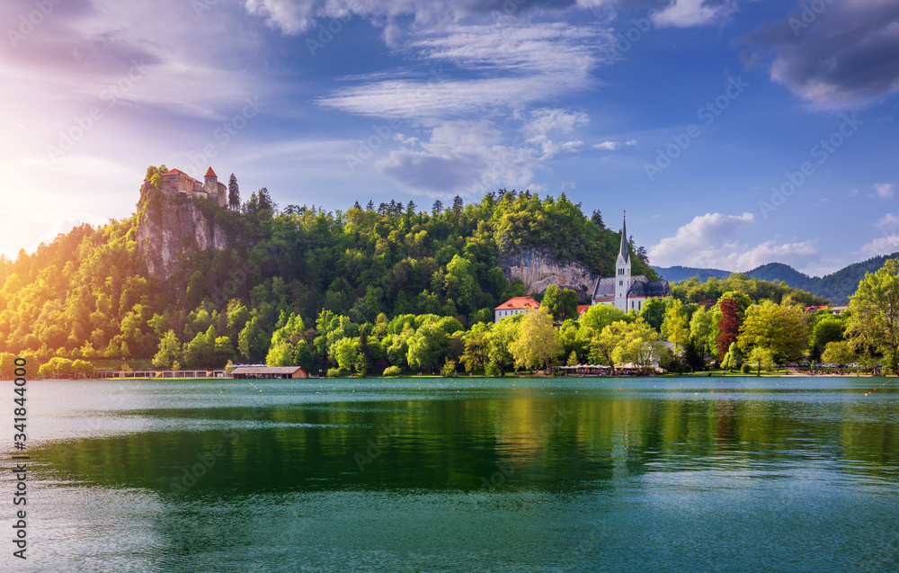 Amazing sunny scenery of Bled castle and St. Martin's Church and Bled town with reflection in the lake and the Julian Alps on background. Bled Lake, Slovenia.