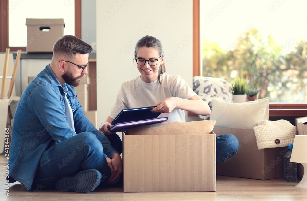 Happy couple looking at photo album while unpacking stuff after relocation to new flat Happy couple looking at photo album while unpacking stuff after relocation to new flat