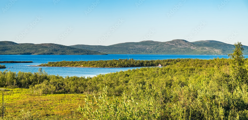 Summer landscape with green medow and lake, forest and village on horizon near Sangis in Kalix Municipality, Norrbotten, Sweden. Swedish landscape in summertime.