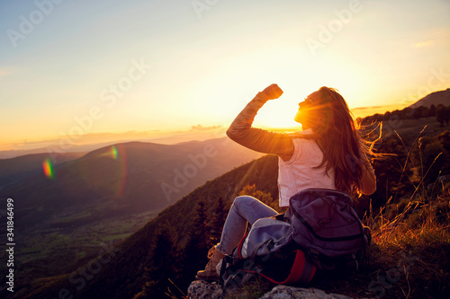 Young woman rise hand up on top of mountain and sunset sky abstract background.
