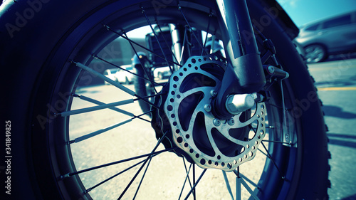 Focus on the tire of the electric bicycle with wheel motor at sunny summer day and light leaks and asphalt on the background. E bike motor with sun reflections on the parking near store. Close up.