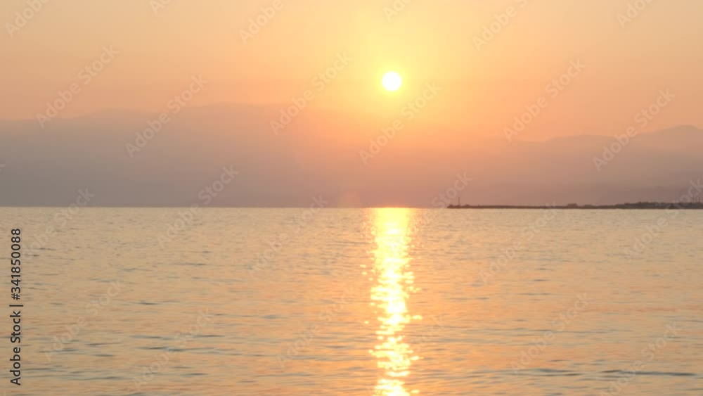 Amazing beautiful sunrise over calm sea. Yellow sun rises above sea and mountains, solar path on water. Sunlight and sun ray reflect on water surface. Golden light, orange and gold blue sky, Panorama Amazing beautiful sunrise over calm sea. Yellow sun rises above sea and mountains, solar path on water. Sunlight and sun ray reflect on water surface. Golden light, orange and gold blue sky, Panorama