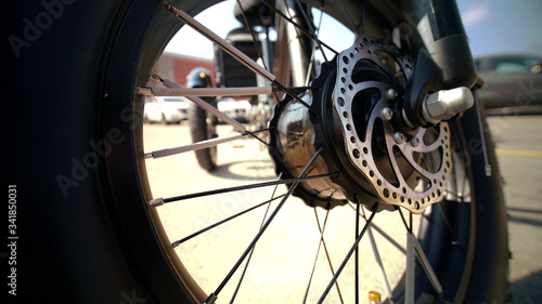 Focus on the tire of the electric bicycle with wheel motor at sunny summer day and light leaks and asphalt on the background. E bike motor with sun reflections on the parking near store. Close up.