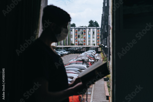 man wearing mask protection and passing quarantina reading books and reflecting at home and looking through the window photo