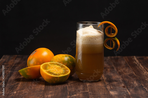 Organic lulo or naranjilla south america exotic fruit. Slice and whole fruits and juice glass on old table and dark background. Solanum quitoense, dark food photo