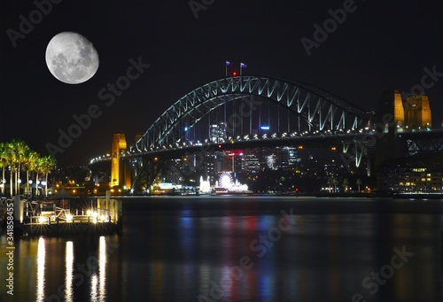 Sydney harbour bridge illuminated by the moon and circular quay with vibrant colourful of the moon and lights at midnight in NSW Australia