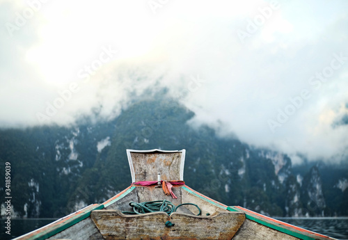 A wooden boat sailing on the lake in front of the beautiful cloudy mountain at Ratchaprapha Dam. photo