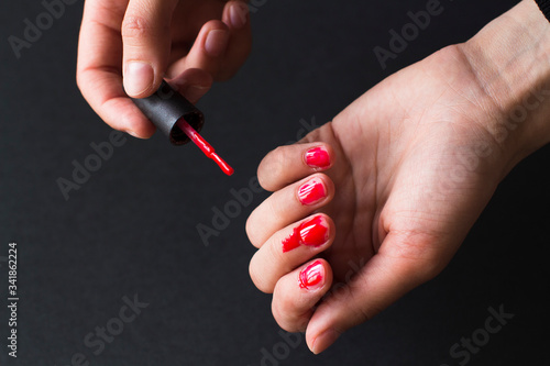 young woman making herself a terrible manicure using red nail polish on black background