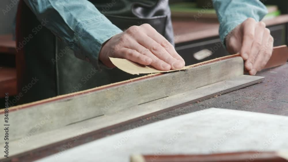 A craftsman is sharpening the edges of a belt. The leather master is making a belt A craftsman is sharpening the edges of a belt. The leather master is making a belt