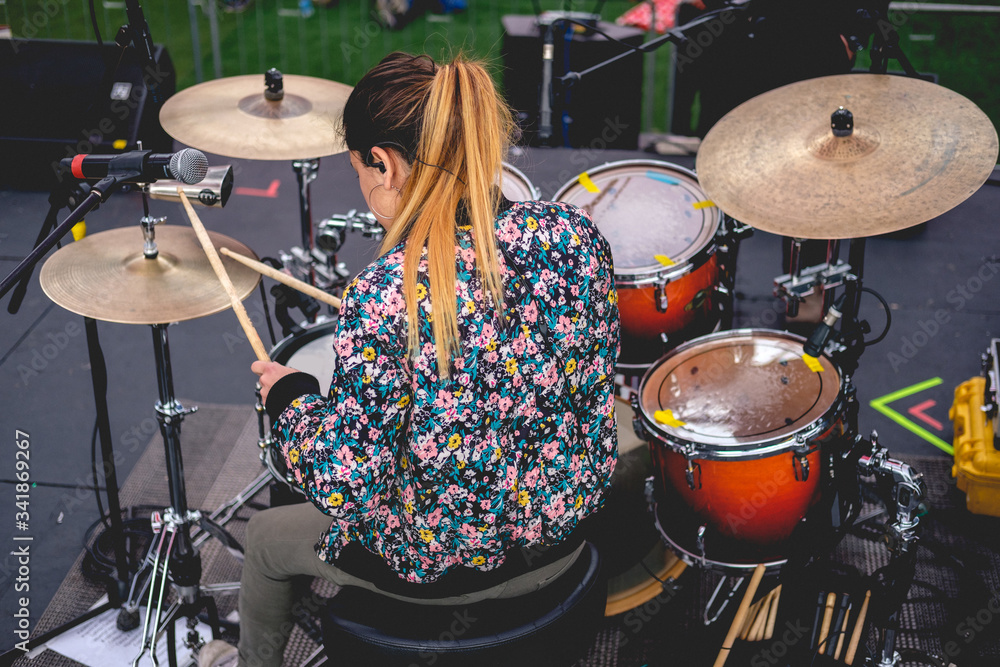Obraz premium Beautiful young blonde drummer from back with drums and flowery sweatshirt playing live on stage