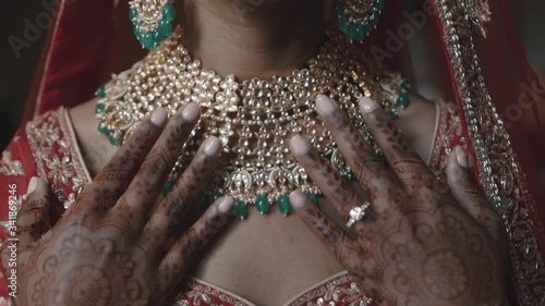 Indian bride is touching precious necklace, dressed in red saree, hands covered with traditional wedding ornamental henna tattoos with engagement ring