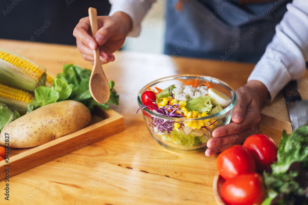 Closeup image of a female chef cooking and holding a bowl of fresh mixed vegetables salad to eat in kitchen
