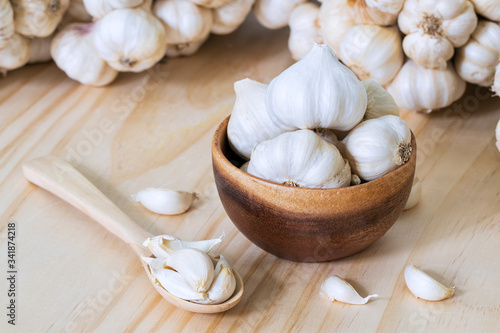 Garlic bulbs in wooden bowl and garlic cloves in wooden spoon on wooden table with garlics blur background..