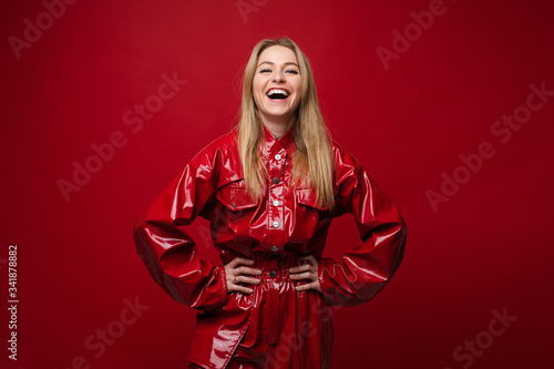 Portrait of handsome caucasian female with long fair hair in red leather costume keeps her hands in the pockets