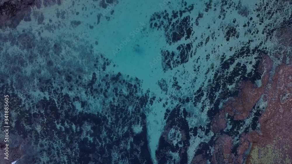 Aerial lock down view: Above the ocean, waves and water surface above coast line