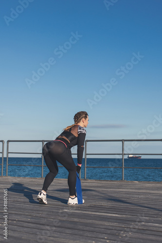 Caucasian female fitness model performing resistance band exercise outdoor at a sea promenade