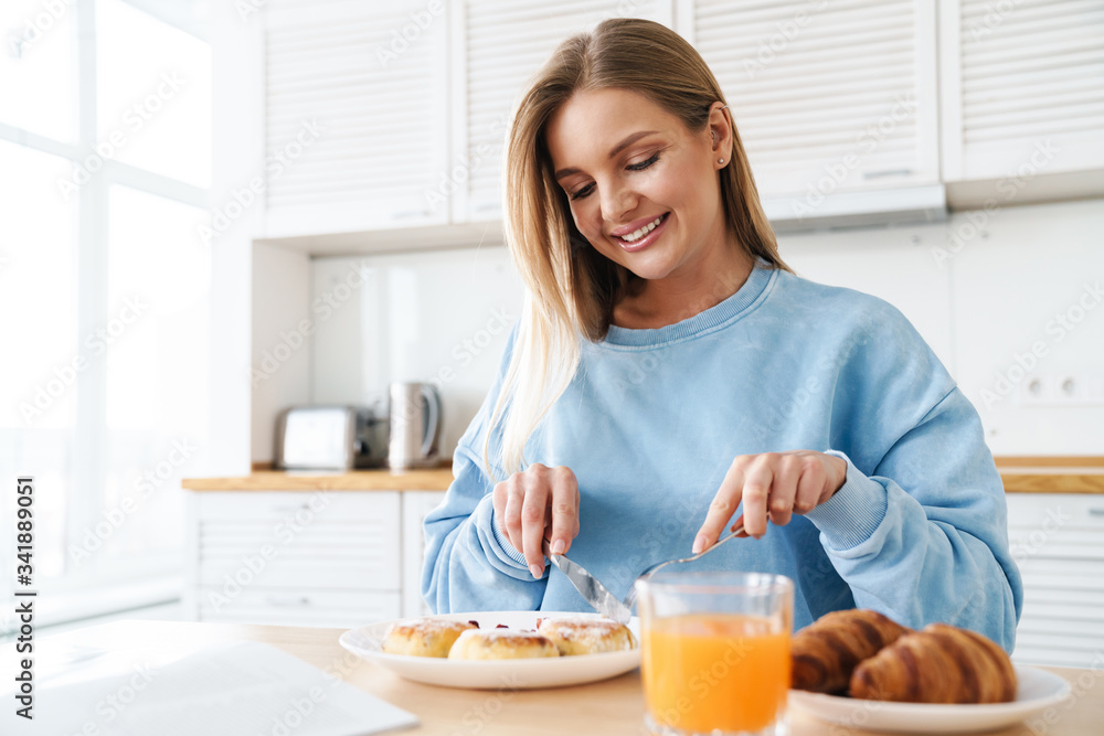Image of cheerful young woman smiling while having breakfast Image of cheerful young woman smiling while having breakfast