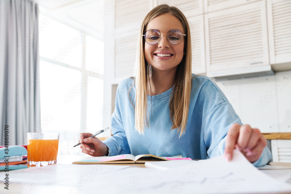 Image of pleased woman smiling while studying with exercise books Image of pleased woman smiling while studying with exercise books