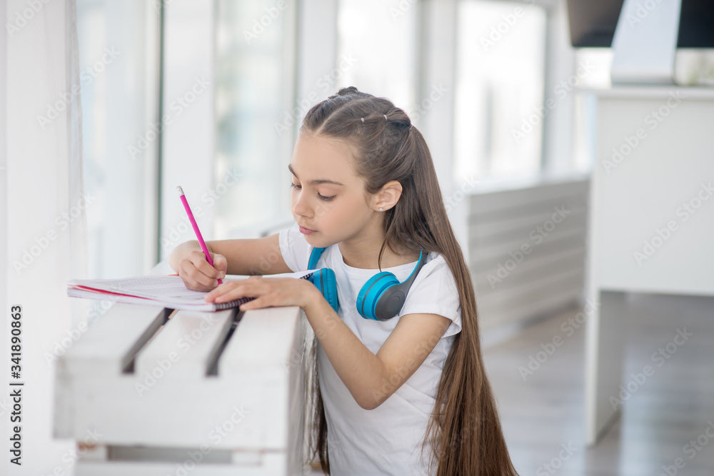 Girl with long hair and earphones around her neck writing something Girl with long hair and earphones around her neck writing something