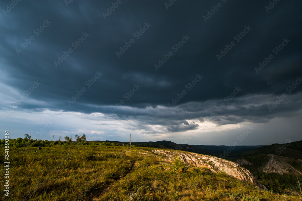 small mountains, illuminated by the setting sun, and storm clouds in the sky