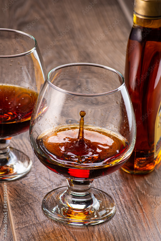 two glasses with cognac and splash next to a bottle on a wooden background two glasses with cognac and splash next to a bottle on a wooden background