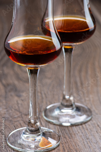 two glasses of sniffer with cognac and waves and splash closeup on wooden background