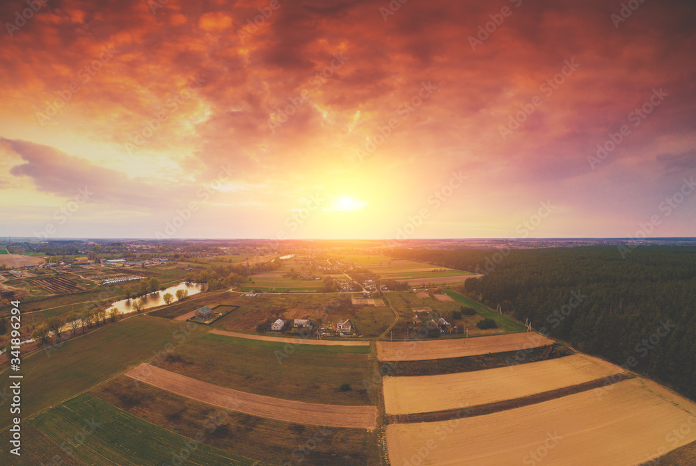 Fototapeta premium Panoramic view from above of countryside, arable fields, and pine forest in the spring evening. Beautiful dramatic sky at a blazing sunset