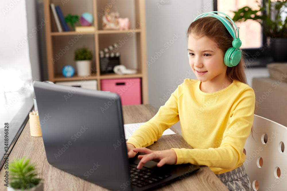 children, education and distant learning concept - little student girl in headphones with laptop computer at home children, education and distant learning concept - little student girl in headphones with laptop computer at home