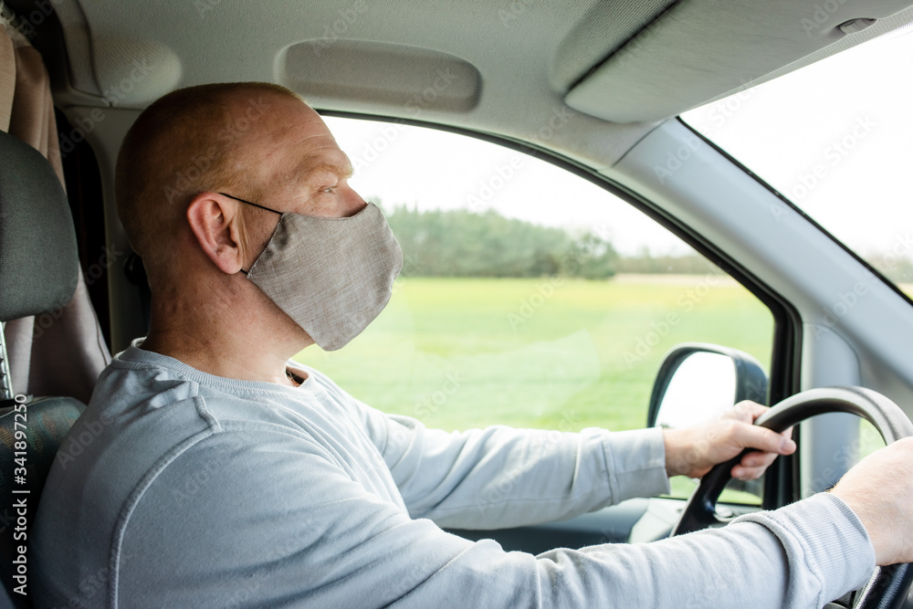 A man in a protective mask driving a car. Portrait of a man in a car in a surgical mask. A man goes to rest in the countryside.