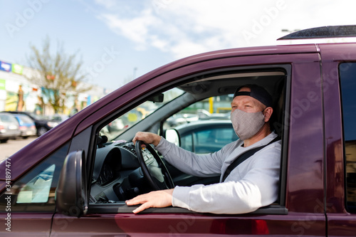 A man in a protective mask driving a car. Portrait of a man in a car in a surgical mask. A man goes to rest in the countryside. © Denys