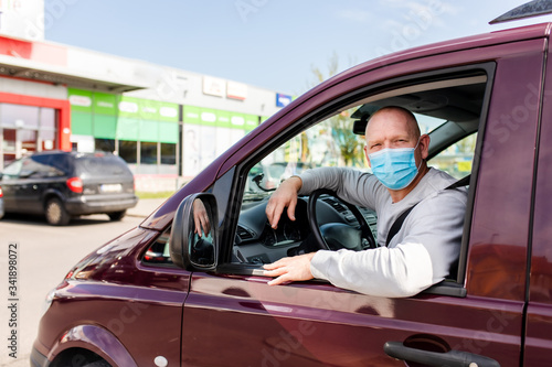 A man in a protective mask driving a car. Portrait of a man in a car in a surgical mask. A man goes to rest in the countryside. © Denys