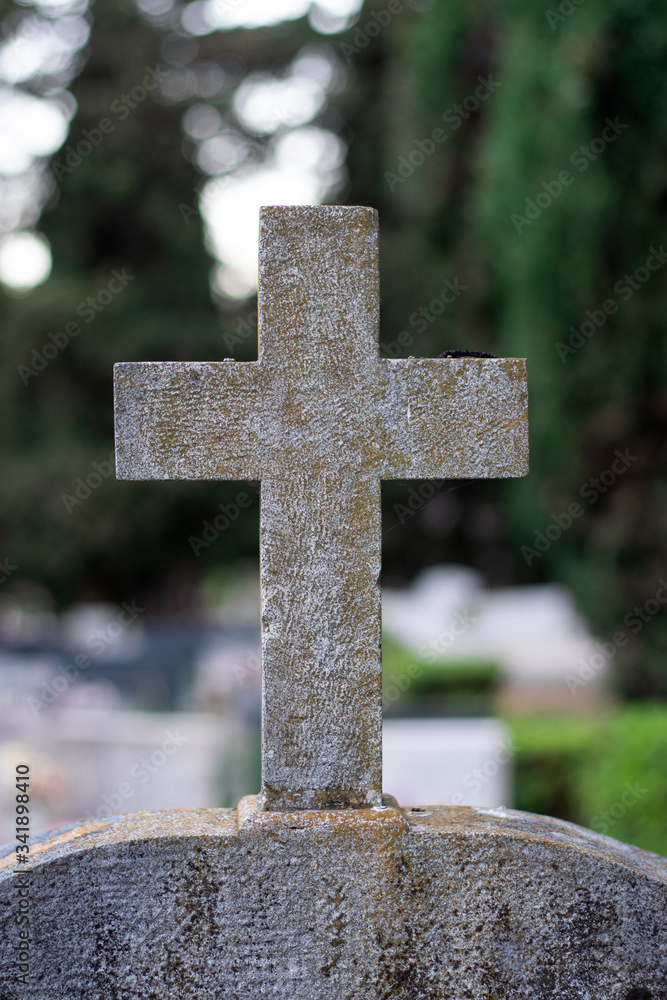 White stone cross with green orange marks worn over time marking a tombstone in a graveyard White stone cross with green orange marks worn over time marking a tombstone in a graveyard