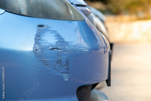 Fotografie Scratch on a bumper of a blue car on a public parking