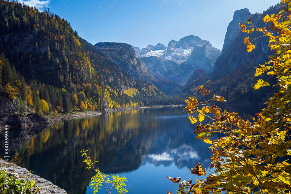 Obraz premium Peaceful autumn Alps mountain lake with clear transparent water and reflections. Gosauseen or Vorderer Gosausee lake, Upper Austria. Dachstein summit and glacier in far.